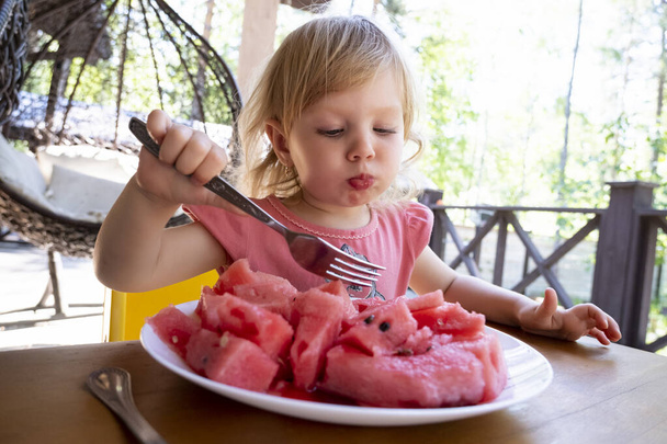 Egy kislány dinnyét eszik a nyári teraszon. - Fotó, kép