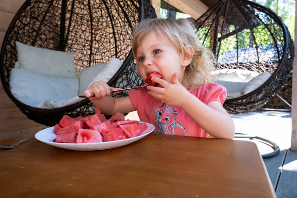 Küçük kız yaz terasında karpuz yiyor. - Fotoğraf, Görsel