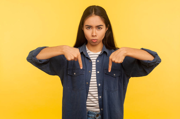 Here and right now! Portrait of girl in denim shirt pointing fingers down, ordering and controlling, demanding result immediately, authority concept. indoor studio shot isolated on yellow background - Photo, Image