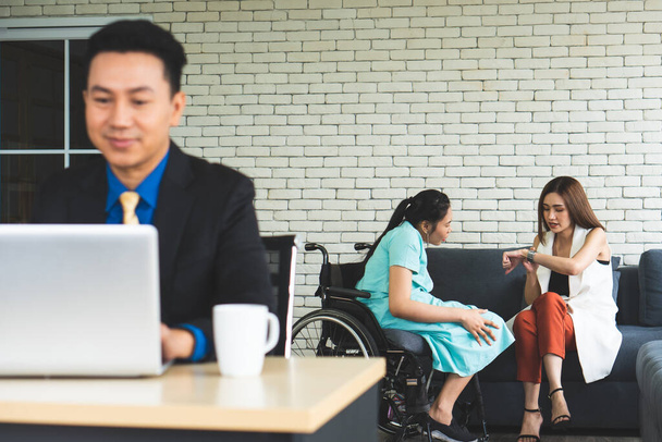 asian businessman working in office while disabled woman and her colleage sitting on the couch. disability and handicapped concept - Fotoğraf, Görsel