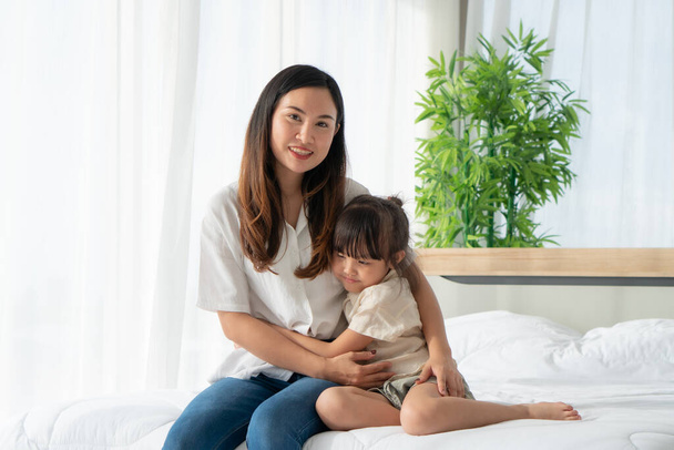 Portret azjatyckiej matki z uśmiechniętą twarzą przytula młodą córkę w sypialni. relacja rodzinna i wspólna koncepcja - Zdjęcie, obraz