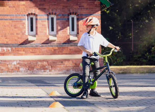Παιδί του σχολείου μαθαίνει να οδηγούν ένα ποδήλατο στο πάρκο, Πορτρέτο του ένα χαριτωμένο μικρό αγόρι με ποδήλατο, Παιδί στο κράνος ιππασία ένα ποδήλατο στο δρόμο. - Φωτογραφία, εικόνα