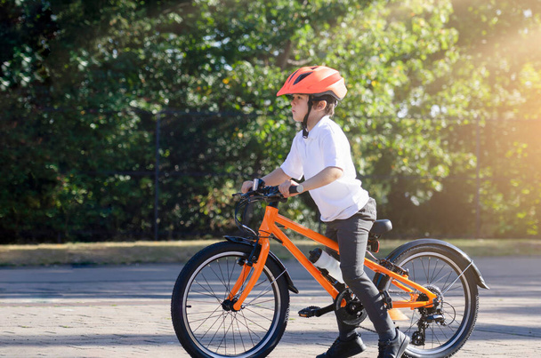 Az iskolás srác biciklizni tanul a parkban, portré egy aranyos kisfiúról kerékpáron, gyerek sisakban biciklizik az úton. - Fotó, kép