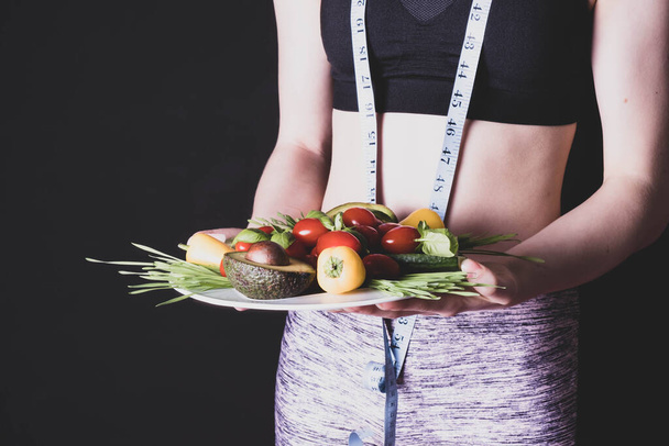 athletic body of a standing young girl and holding a plate with fresh vegetables - Foto, immagini