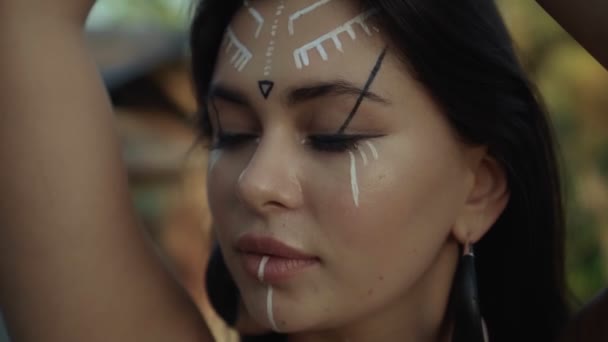 Video of a beautiful young brunette European girl with makeup and painted ethnic lines on the body walking in a tropical garden - Filmmaterial, Video