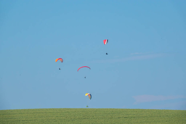 sobre um campo verde no horizonte voar diferentes parapentes
 - Foto, Imagem