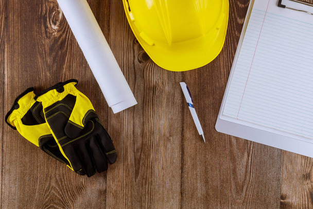 建築設計図の家の計画のロールに取り組む建設事務所のエンジニアは、木製の背景に黄色のヘルメットの安全保護手袋を作業 - 写真・画像