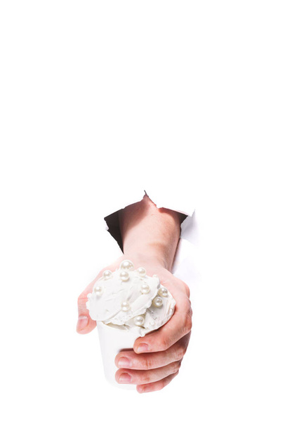 main masculine avec crème glacée blanche avec des perles douces à travers un trou dans le papier sur un isolat de fond blanc. gros plan, espace de copie. - Photo, image