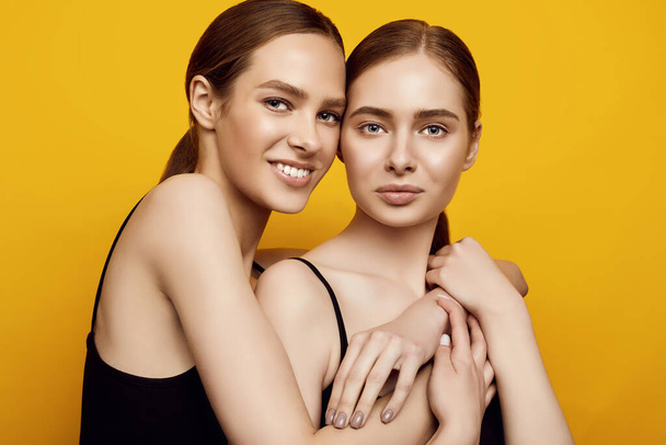 Portrait of lovable two caucasian girls expressing positive emotions to camera isolated on yellow background in studio - Photo, Image