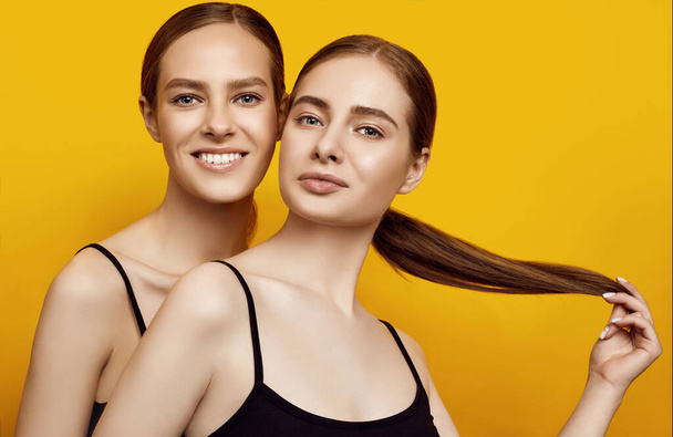 Portrait of lovable two caucasian girls expressing positive emotions to camera isolated on yellow background in studio - Photo, Image