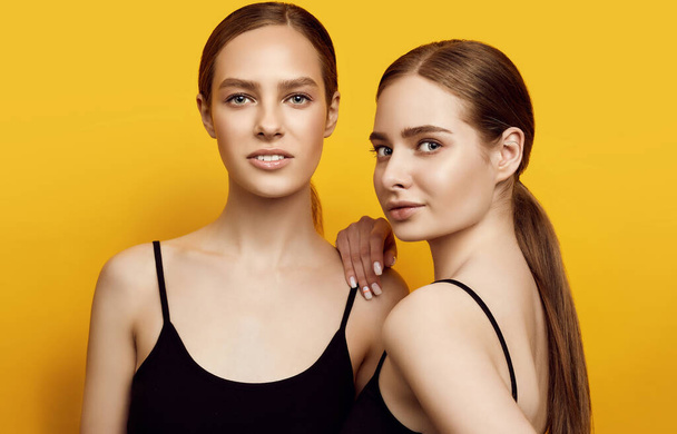Stüdyoda sarı arka planda izole edilmiş, olumlu duygularını ifade eden iki beyaz kızın portresi. - Fotoğraf, Görsel