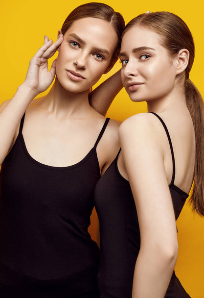 Muotokuva rakastettavista kahdesta valkoihoisesta tytöstä, jotka ilmaisevat positiivisia tunteita keltaisella taustalla eristettyyn kameraan studiossa - Valokuva, kuva