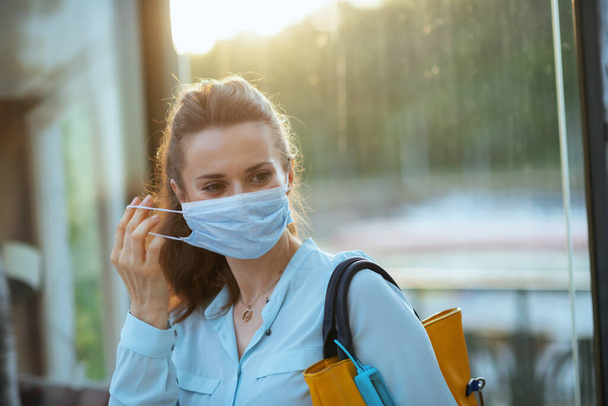 Life during coronavirus pandemic. young woman in blue blouse with medical mask wearing medical mask at the bus stop outdoors on the city street. - Foto, imagen