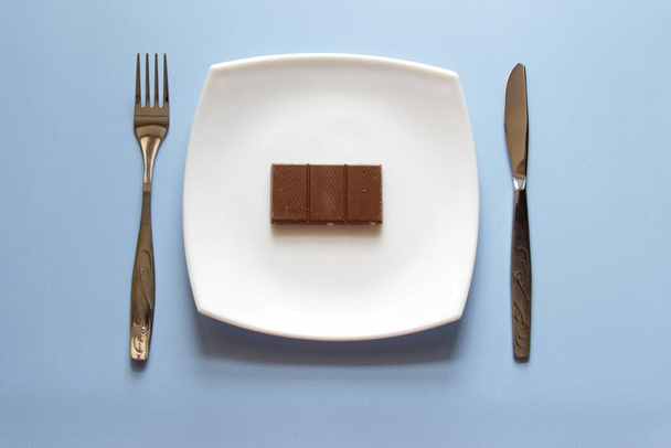 Fork, knife and white plate with chocolate over blue background. Clean plate and cutlery on light background. Top view. - Fotó, kép