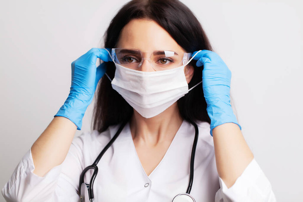 Female doctor in a white coat puts a surgical mask on his face - Zdjęcie, obraz