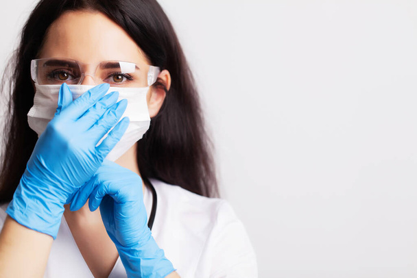 Female doctor in a white coat puts a surgical mask on his face - Foto, Imagem