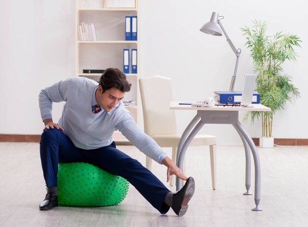 Employee exercising with swiss ball during lunch break - Foto, Imagen