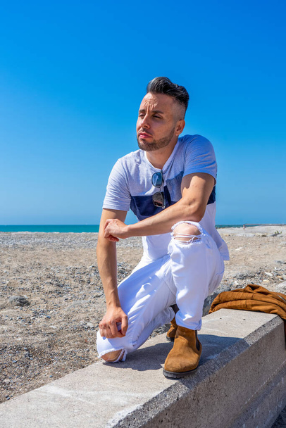 Young man in white pants and modern styling posing on the beach of the Mediterranean Sea in Burriana. Fashion concept - Фото, зображення
