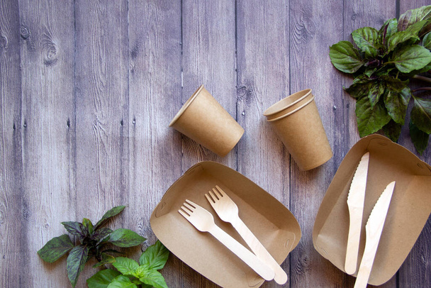 Eco friendly, disposable, recyclable, compostable tableware. Paper food boxes, dishes and fresh basil leaves on a wooden background. Sustainable lifestyle concept.  Flat lay, copy space. - Photo, Image