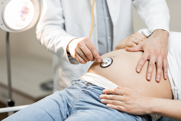 Doctor listening to a pregnant womans belly - Foto, afbeelding