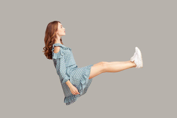 Hovering in air. Full length side view of calm serious brunette pretty girl ruffle dress levitating, looking away with concentrated focused pensive expression. studio shot isolated on gray background - Фото, изображение