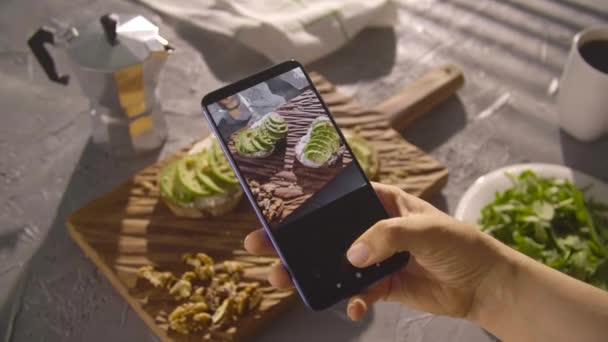 Zdravý stravovací koncept. Ruční fotografování sendvič s avokádem s chytrým telefonem - Záběry, video