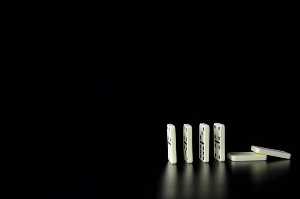 Bloques de dominó blanco mirando hacia una dirección y colocados en una línea recta con dos bloques acostados sobre fondo negro
 - Foto, imagen