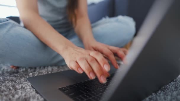 女性は床に座ってノートパソコンで作業しています。リモートワークの概念. - 映像、動画
