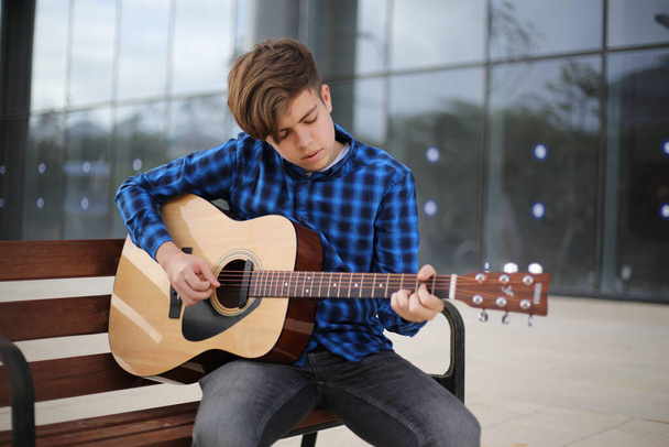 Ragazzo adolescente che suona la chitarra all'aperto. Imparare a suonare la chitarra. Educazione musicale. - Foto, immagini