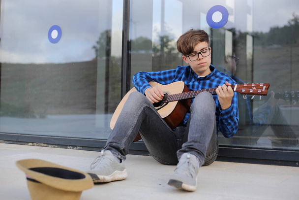 Tiener jongen speelt gitaar buiten. Gitaarleren spelen. Muziekonderwijs. - Foto, afbeelding