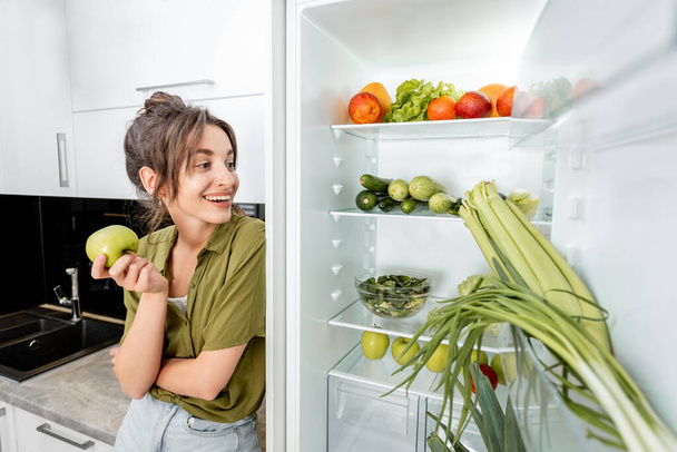 Woman near the fridge full of healthy food - Photo, Image