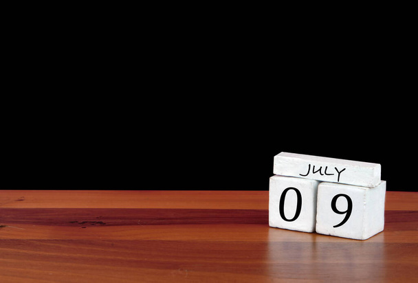 9 juli kalendermaand. Negen dagen van de maand. Reflecterende kalender op houten vloer met zwarte achtergrond - Foto, afbeelding