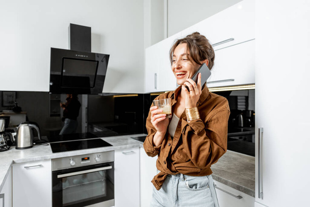 Frau mit Telefon und Kaffee in der modernen Küche zu Hause - Foto, Bild