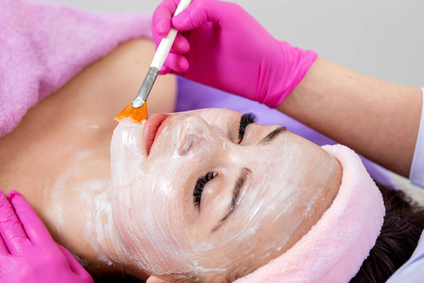 Face peeling mask, spa beauty treatment, skincare. Woman getting facial care by beautician at spa salon, side view, close-up. Anti-aging treatment. Cosmetology and professional facial skin care - Foto, immagini