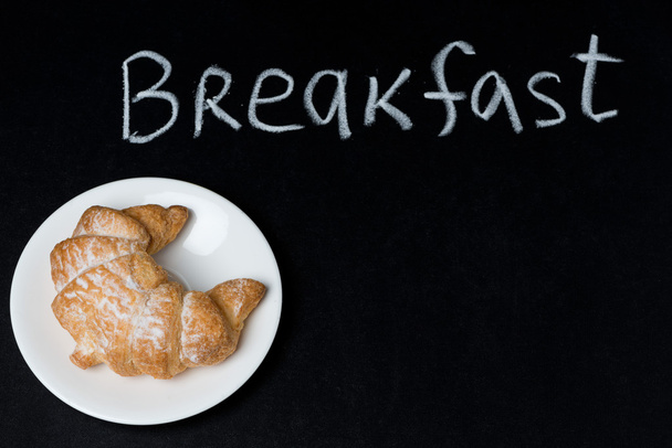 Croissant on a plate on the blackboard and the word breakfast - Фото, зображення