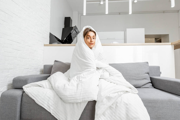 Γυναίκα σκεπασμένη με κουβέρτα στον καναπέ στο σπίτι. - Φωτογραφία, εικόνα