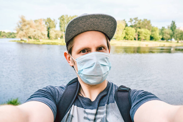 Şehirdeki bir salgın sırasında tıbbi maske takmış beyaz bir adamın portresi selfie çekiyor. Yeni normal. - Fotoğraf, Görsel