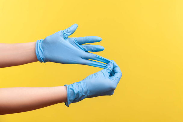 Profile side view closeup of human hand in blue surgical gloves showing how to take of gloves. indoor, studio shot, isolated on yellow background. - Foto, afbeelding