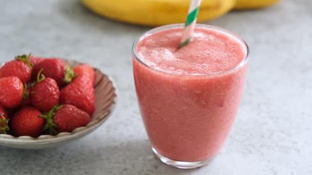 Strawberry smoothie in glass cup with paper drinking straw. Fresh raw vegetarian strawberry smoothie - Filmati, video