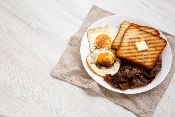 Hausgemachtes gesundes Sunnyside Eggs Frühstück auf einem weißen Teller auf weißem Holzhintergrund, Blick in den niedrigen Winkel. Kopierraum. - Foto, Bild