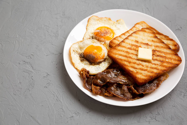 Hausgemachtes gesundes Sunnyside-Ei-Frühstück auf einem weißen Teller auf einer grauen Oberfläche, flache Sicht. Kopierraum. - Foto, Bild