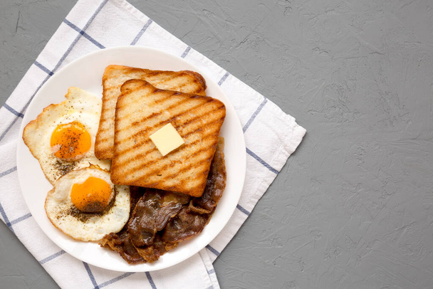 Hausgemachtes gesundes Sunnyside Eggs Frühstück auf einem weißen Teller auf einer grauen Oberfläche, Draufsicht. Flach liegend, über Kopf, von oben. Kopierraum. - Foto, Bild