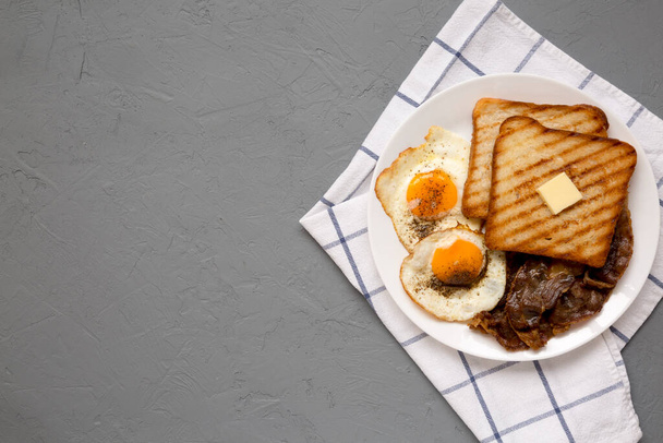 Hausgemachtes gesundes Sunnyside Eggs Frühstück auf einem weißen Teller auf grauem Hintergrund, Draufsicht. Flach liegend, über Kopf, von oben. Kopierraum. - Foto, Bild