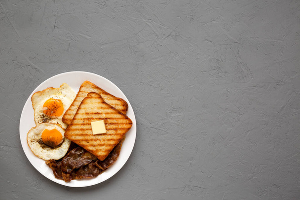 Hausgemachtes gesundes Sunnyside Eggs Frühstück auf einem weißen Teller auf einer grauen Oberfläche, Blick von oben. Flach liegend, über Kopf, von oben. Kopierraum.  - Foto, Bild