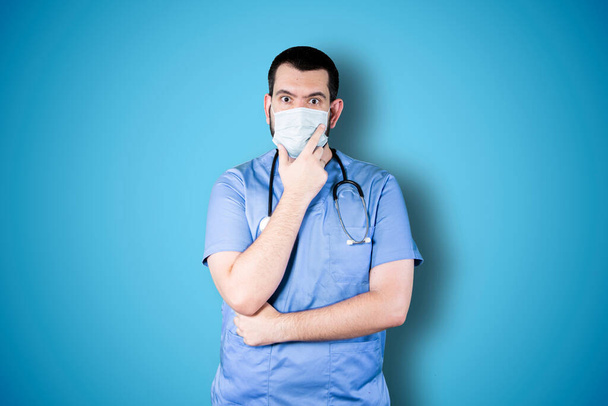 Handsome doctor with mask isolated on blue background thinking an idea while looking up - Photo, image
