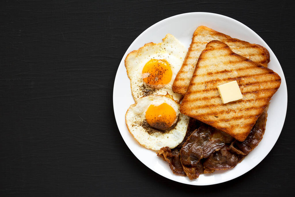 Домашний здоровый завтрак "Яйца Саннисайд" на белой тарелке на черной поверхности, вид сверху. Плоский лежал, над головой, сверху. Копирование пространства
. - Фото, изображение