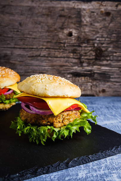 Two Fresh delicious homemade veggie burger lies on natural slate on rustic wooden background. Delicious tasty burger with lettuce, cheese, onion and tomato. buckwheat and lentil cutlet. Vertical orintation. - Photo, image