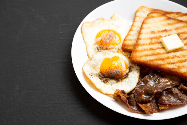 Hausgemachtes gesundes Sunnyside-Ei-Frühstück auf einem weißen Teller auf schwarzer Oberfläche, Blick in den niedrigen Winkel. Raum für Text. - Foto, Bild
