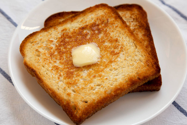 Домашний тост с маслом на белой тарелке с низким углом обзора. Крупный план
. - Фото, изображение