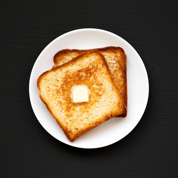 Homemade Buttered Toast on a white plate on a black surface, top view. Flat lay, overhead, from above.  - Photo, Image